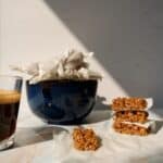 blue bowl full of wrapped grape nuts pasteli. 4 unwrapped outside the bowl next to an espresso.