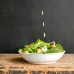 Modern Caesar salad in a white bowl with an eggless salad dressing being poured on top