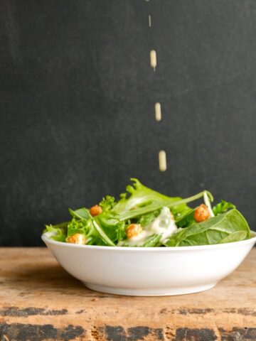 Modern Caesar salad in a white bowl with an eggless salad dressing being poured on top