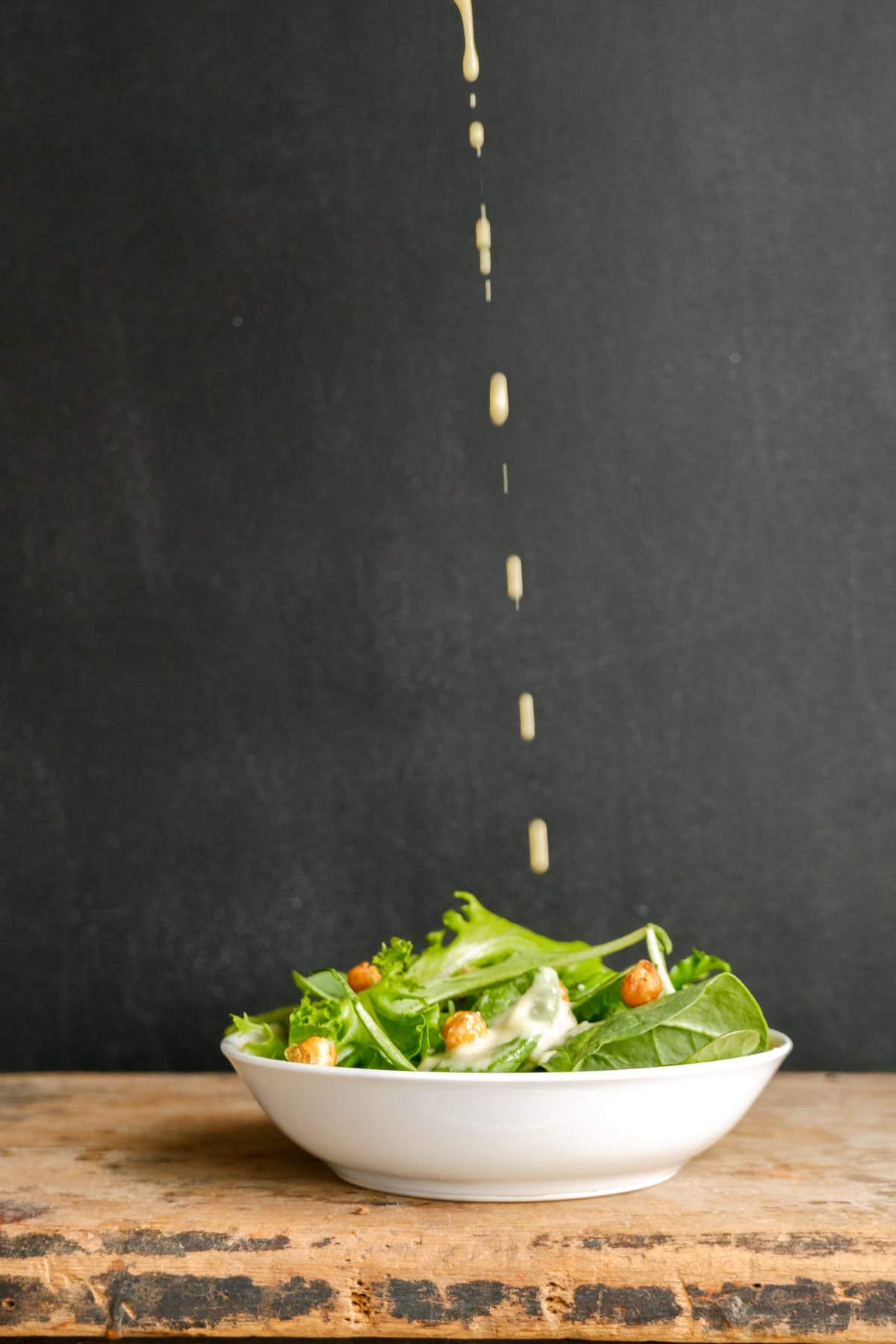 Modern Caesar salad in a white bowl with an eggless salad dressing being poured on top