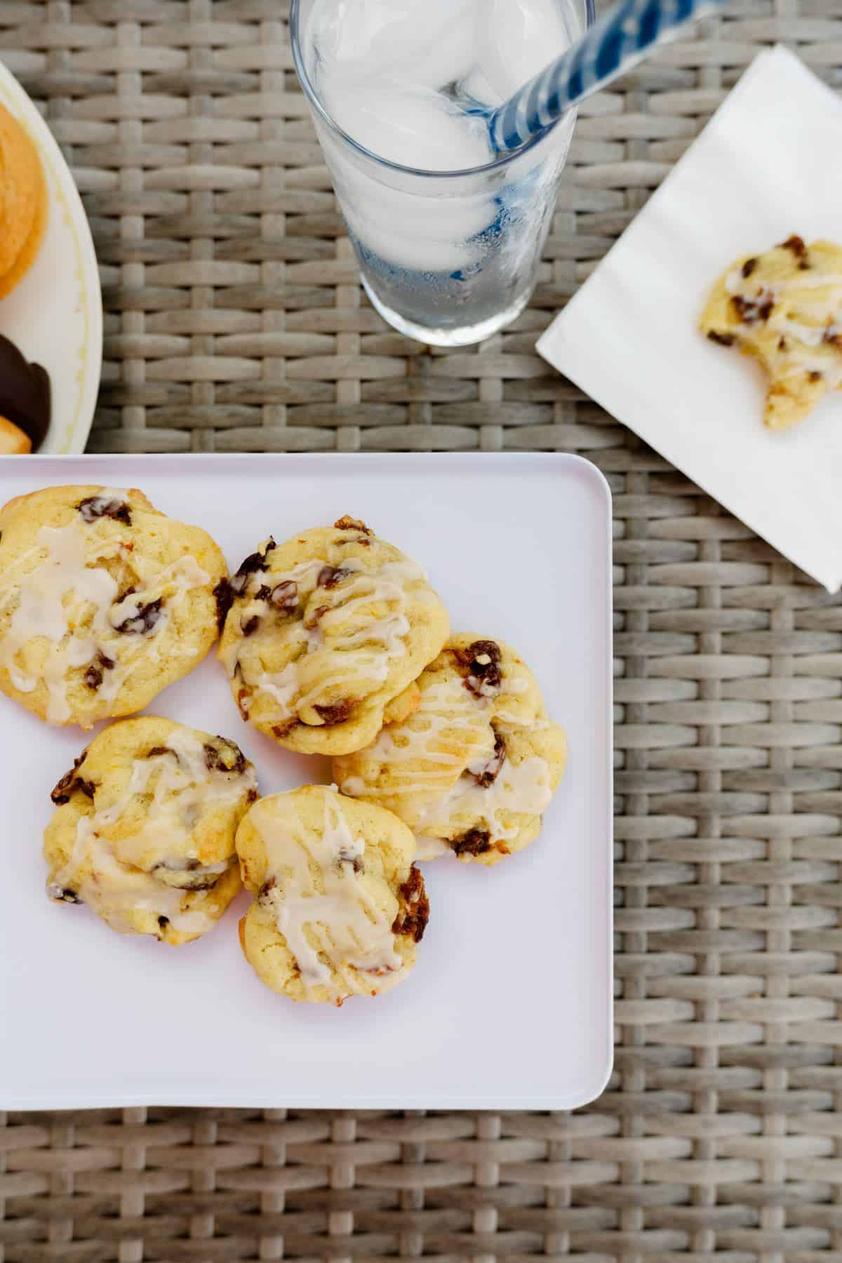 plated outdoor scene of 5 iced orange rum raisin cookies with a glass and colored straw