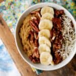 Whole30 sweet potato breakfast bowl close up. On bed tray. Topped with bananas, coconut flakes, dates and pecans.