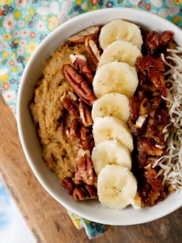 Whole30 sweet potato breakfast bowl close up. On bed tray. Topped with bananas, coconut flakes, dates and pecans.