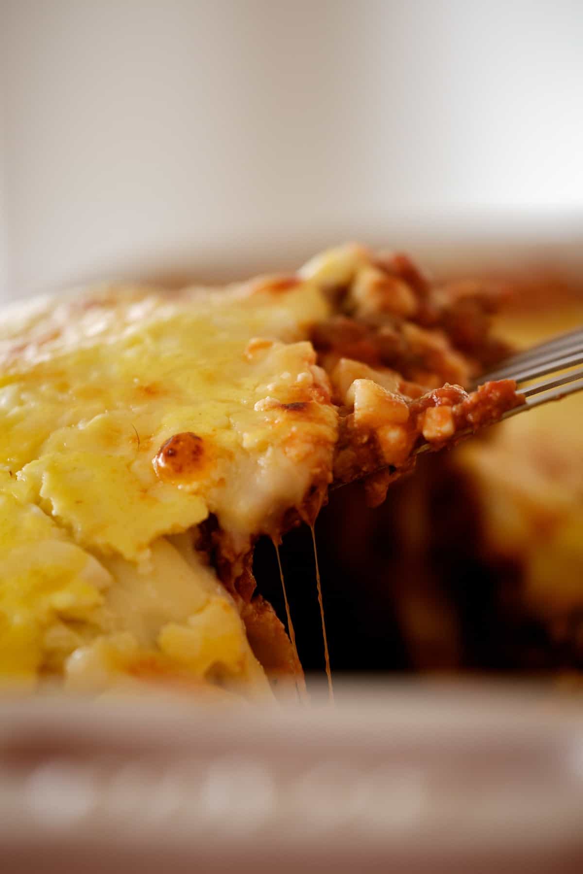 spatula pulling cheesy lasagna out of the pan