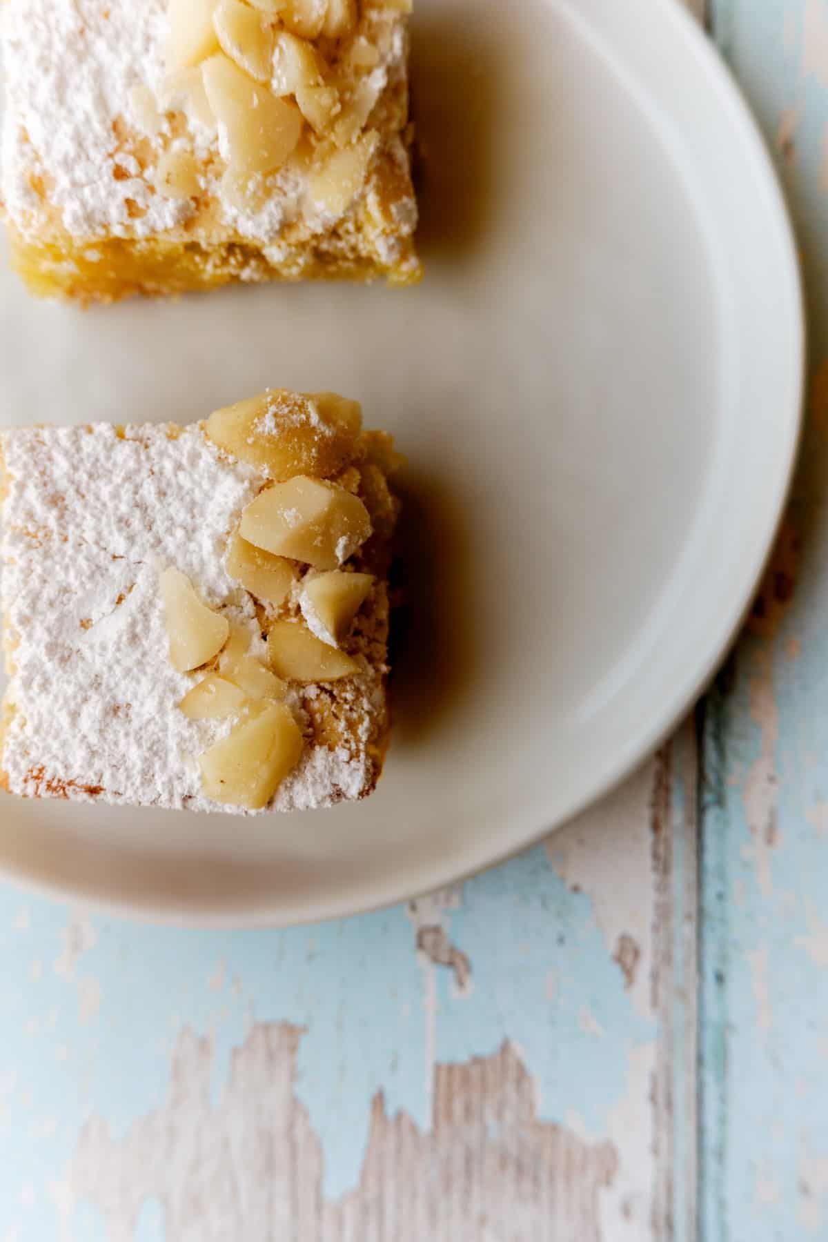 2 lemon squares viewed from straight above on a plate on a rutic wood and blue table