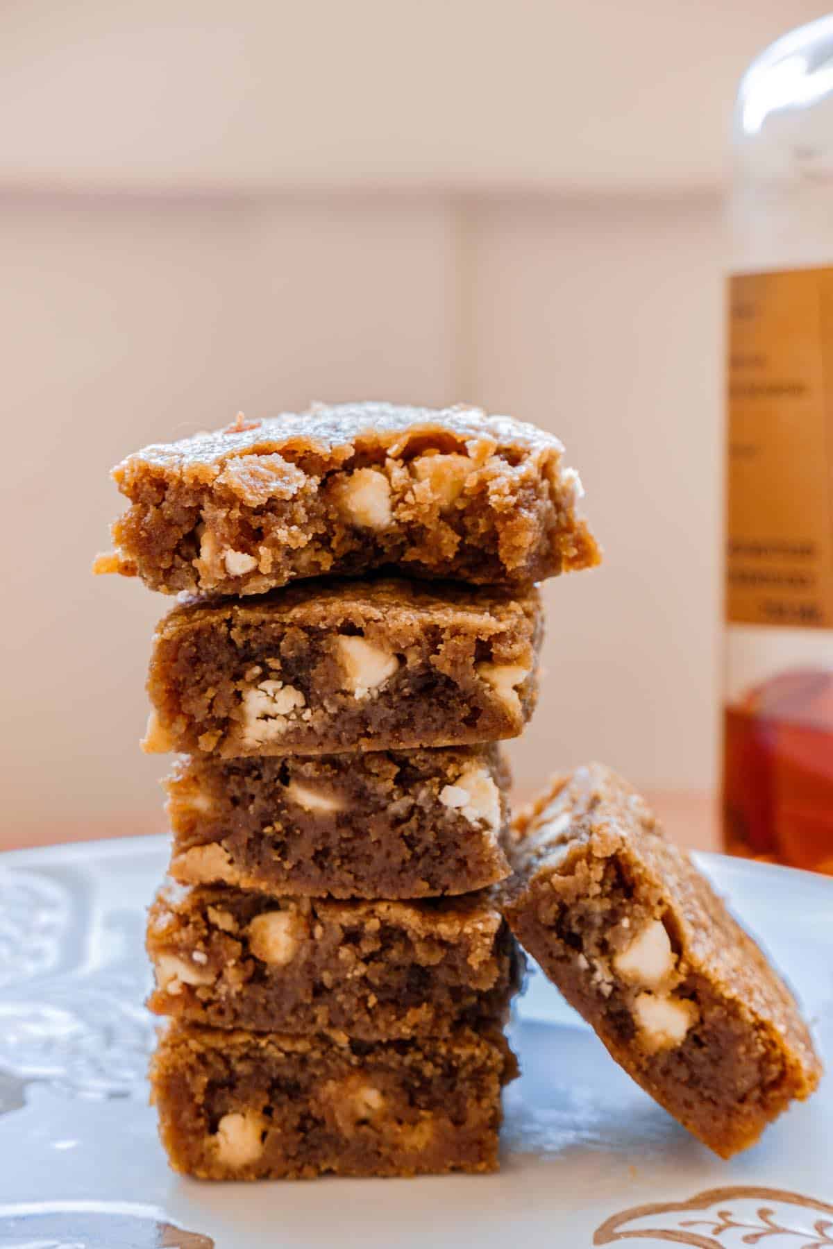 5 stacked bourbon brown butter blondies. Next to a bottle of bourbon and a 6th blondie on its side.