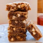 5 stacked bourbon brown butter blondies. Next to a bottle of bourbon and a 6th blondie on its side.