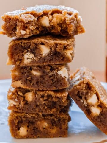 5 stacked bourbon brown butter blondies. Next to a bottle of bourbon and a 6th blondie on its side.